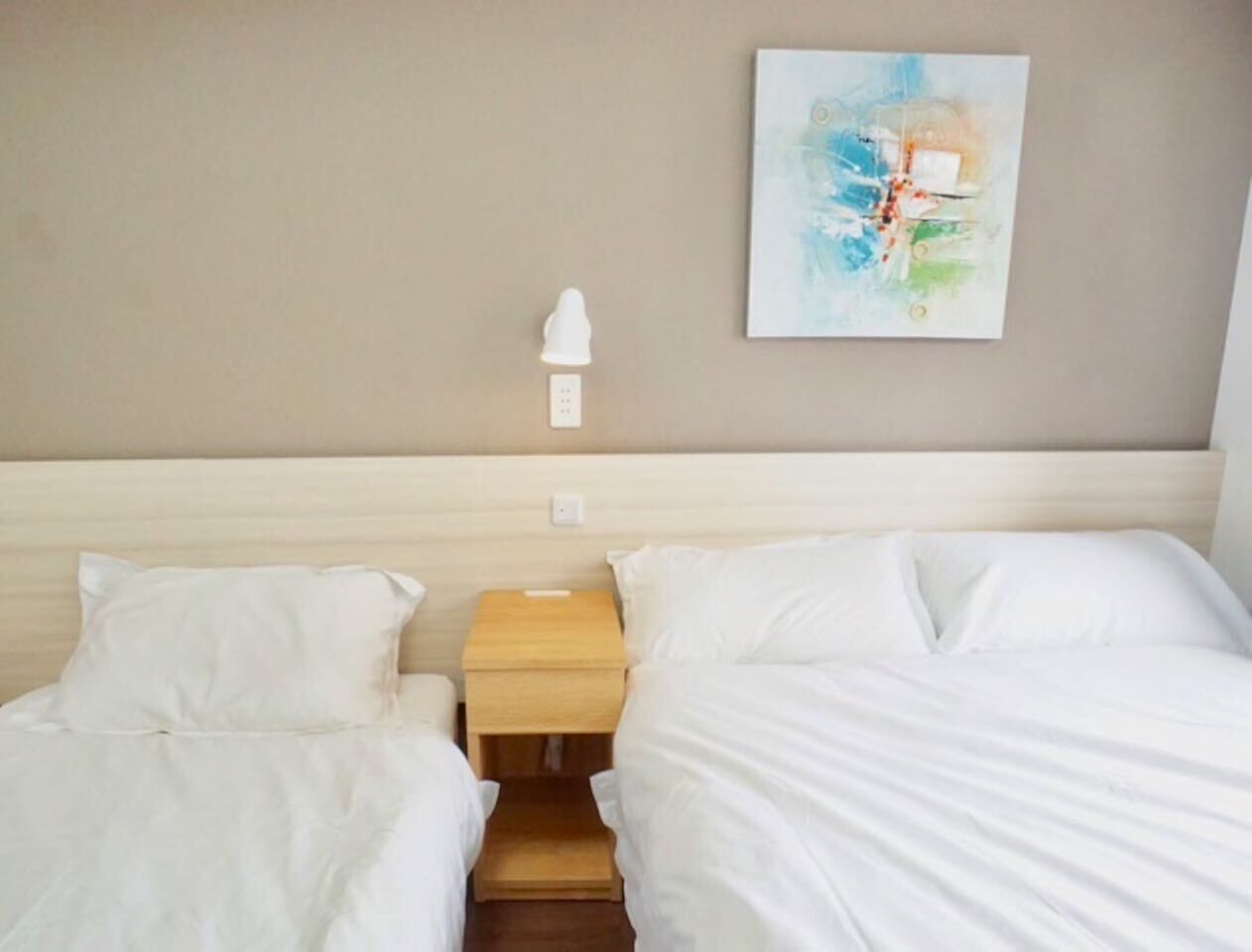 A hotel room with two beds, a nightstand, a wall-mounted lamp, and a painting.