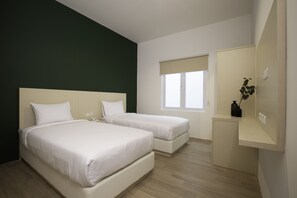 Quarto de hotel com duas camas, uma janela com persiana bege, uma escrivaninha pequena e um espelho.