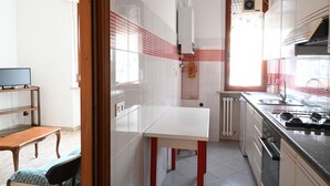 Una cucina compatta con un piano di lavoro bianco, gambe rosse, un fornello e una finestra.