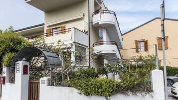 Un immeuble résidentiel à plusieurs étages, doté de balcons, d’une entrée sécurisée et d’un passage couvert pour les voitures.