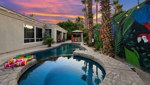 A swimming pool with a stone border, surrounded by palm trees and a mural.