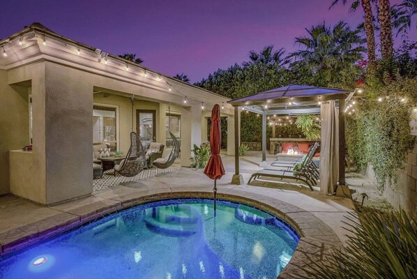 A pool area with a hot tub, lounge chairs, and a covered seating area.