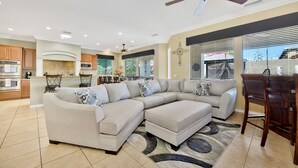 A spacious living room with a large sectional sofa, a dining area with wooden chairs, and a kitchen with modern appliances.