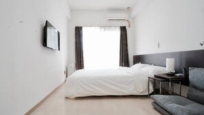 Une chambre d’hôtel comprenant un lit, une table de chevet avec une lampe, un canapé et un appareil de climatisation.