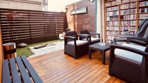 Un espace extérieur aménagé en terrasse, avec des meubles en osier, une petite table et une bibliothèque remplie de livres.