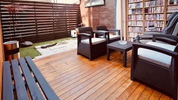 An outdoor patio area with wicker furniture, a small table, and a bookshelf filled with books.