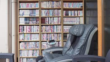 A room with a massage chair, a bookshelf filled with books, and a wooden table.