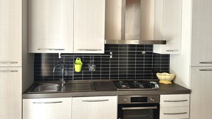 A modern kitchen with stainless steel appliances, a black tiled backsplash, and light-colored cabinetry.