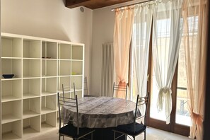 A dining area with a round table, chairs, a white shelving unit, and sheer curtains.