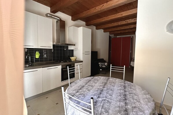 A compact kitchen with white cabinets, a black tiled backsplash, and a red door in the background.