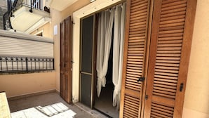 A balcony with a metal railing, a wooden table, and a sliding glass door with wooden shutters.