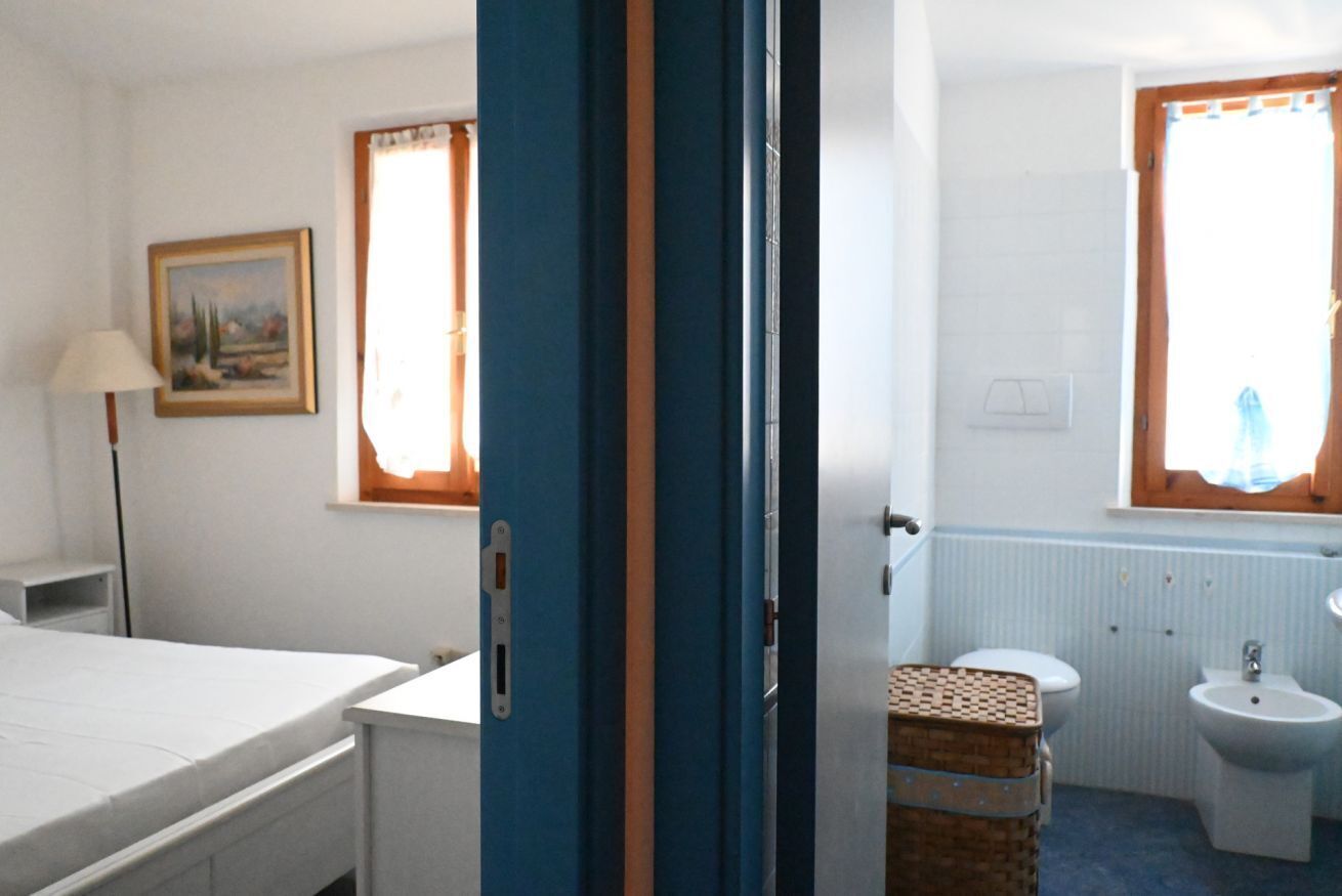 Une chambre comprenant un lit, un bureau, une lampe, un tableau, une fenêtre et une salle de bain avec des toilettes, un bidet et un lavabo.