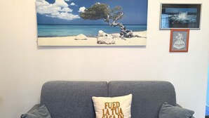 A grey sofa with a cushion that reads 'FUED LA TUA CASA IN VACANZA' and a framed picture of a beach scene above it. - M244 - Marcelli, three-room apartment with terrace 150m from the sea (Marcelli)