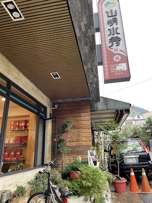Hotel entrance with a modern design and sloped roof, featuring a glass door and potted plants.
