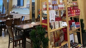 Interior de restaurante con mobiliario de madera, un televisor montado en la pared y estantes repletos de diversos alimentos.