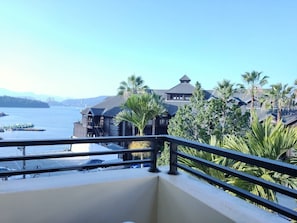 Enjoy a waterfront view from this property's balcony, overlooking a serene water body with lush greenery and boats docked.