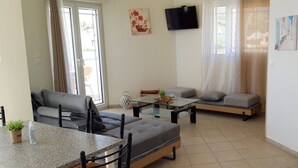 A modern living room with a sofa, a glass-top table, and a TV mounted on the wall. - Makrigialos: big family apartment, 2 bedrooms, sea views, WiFi (Makrigialos)