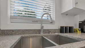 Cocina con lavamanos doble, encimera de granito y ventana con persianas.