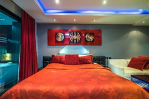 A modern hotel room with a large bed, red bedding, a white sofa, and a wall with three framed artworks. - Absolute Bangla Suites by Lofty (Patong)