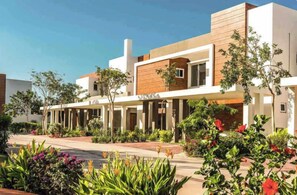 A modern building with a covered walkway, surrounded by landscaped gardens and various plants. - Casa Moderna en Mérida: Alberca Privada, WiFi y 3 Habitaciones (Mérida)