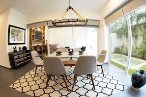 A modern dining area with a glass table, four chairs, and a chandelier.