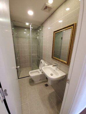 Ein modernes Badezimmer mit Duschkabine aus Glas, Toilette und Waschbecken mit großem Spiegel.