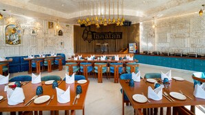 A restaurant with a central bar, blue upholstered seating, and a decorative wall with the name 'Tanatam'.