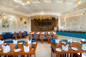 A restaurant with a central bar, blue upholstered seating, and a decorative wall with the name 'Tanatam'.