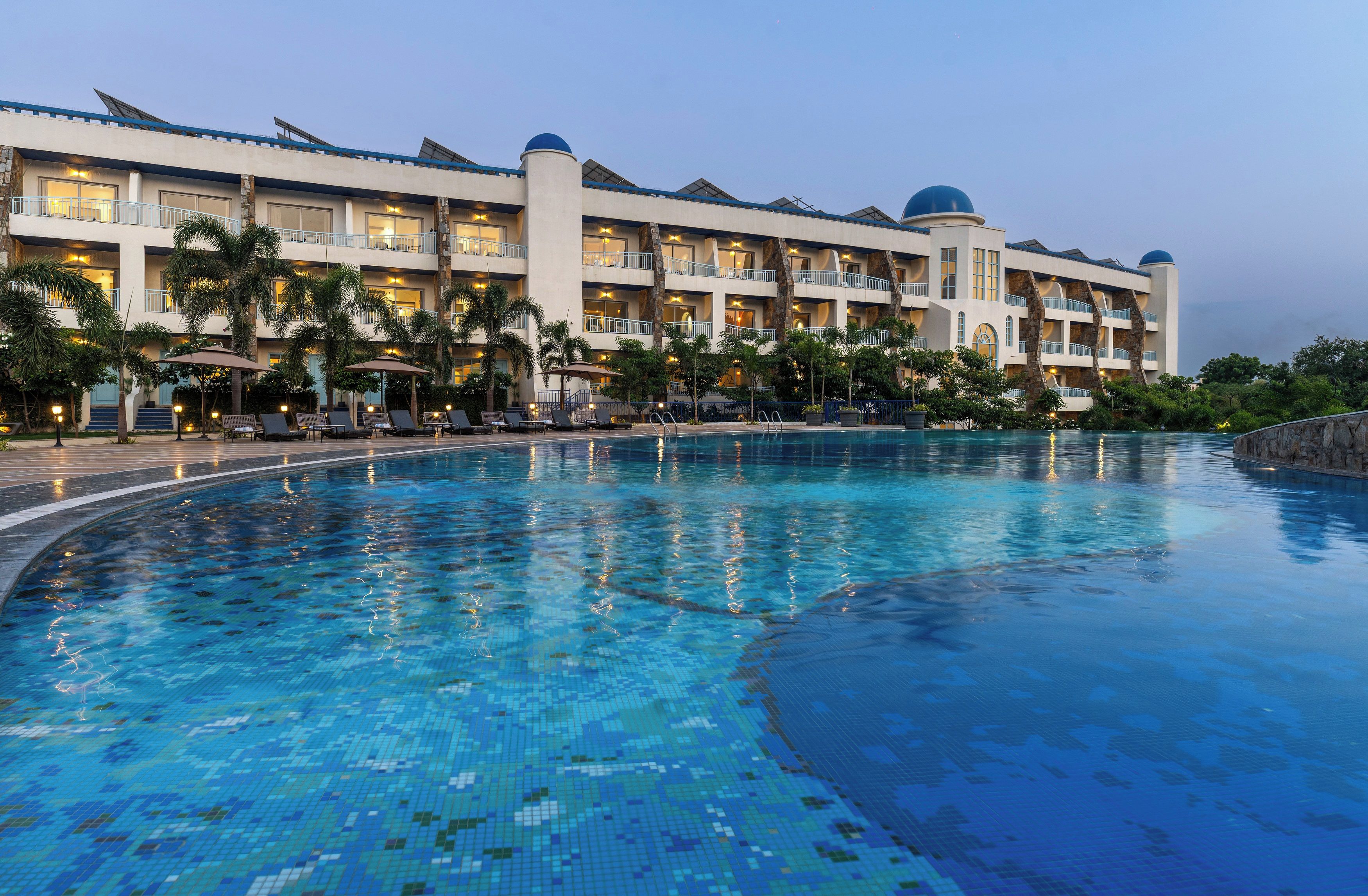 A hotel with a large swimming pool, multiple balconies, and palm trees.