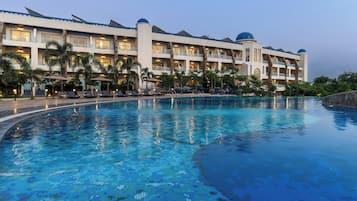 A hotel with a large swimming pool, multiple balconies, and palm trees.