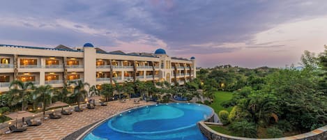 A hotel with a swimming pool, multiple balconies, and lush greenery.