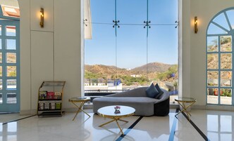 Una sala de estar moderna con sofá, mesa de centro y vistas a un paisaje montañoso a través de amplias ventanas.