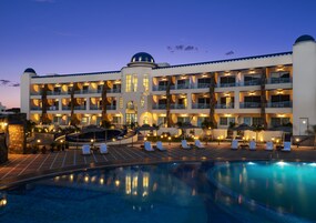 Un hotel con una piscina amplia, varios balcones y una torre central.
