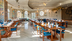 Ein großzügiger Speisebereich mit langen Holztischen und blau gepolsterten Stühlen, verziert mit aufwendigen Wandornamenten und großen Fenstern für natürliches Licht.