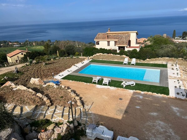 Una piscina con sillas de descanso, un camino de piedra y vista al mar.