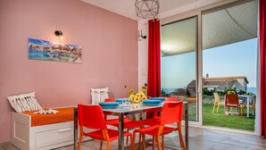 A room with a bed, a dining table with chairs, a painting on the wall, and a view of the outside. - Apt Mari E Monti A 2 Km Da Riserva Dello Zingaro (Castellammare del Golfo)