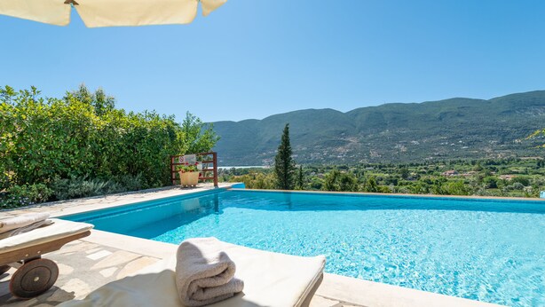 A swimming pool with a view of mountains, a lounge area with a towel, and a pergola with a table and chairs. - Kerithra Villa, overlooking Vasiliki bay, close to the beach and other amenities (Lefkada)
