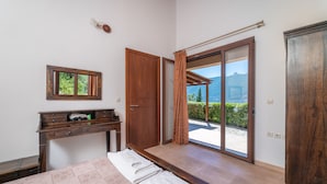 A bedroom with a bed, a wooden desk, a mirror, and a sliding glass door leading to a balcony with a mountain view. - Kerithra Villa, overlooking Vasiliki bay, close to the beach and other amenities (Lefkada)