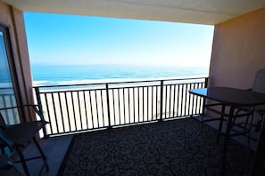 A balcony with a view of the ocean, a table, and two chairs.