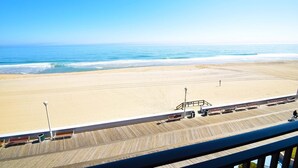 A beach view from a balcony with a wooden deck, a lifeguard tower, and beach chairs. - Ocean Hideaway (Ocean City)