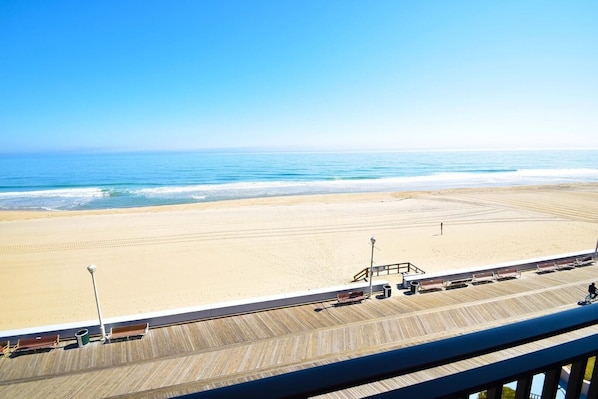 A beach view from a balcony with a wooden deck, a lifeguard tower, and beach chairs.