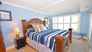 A bedroom with a wooden four-poster bed, a nightstand with a lamp, and a window with blinds. - Ocean Hideaway (Ocean City)