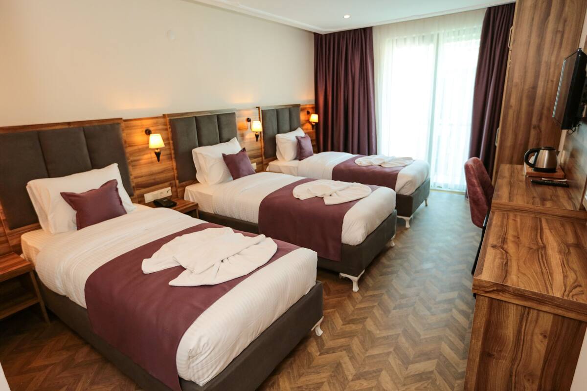 A hotel room with two beds, wooden headboards, and a wooden desk with a kettle.