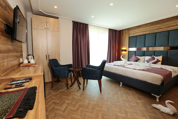 A hotel room with a bed, two chairs, a small table, a TV, and a wardrobe. - Royal Palas Hotel (Van)