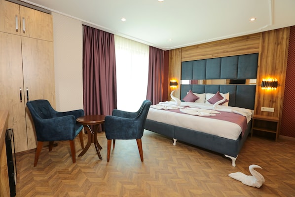 Habitación de hotel con cama, dos sillones azules, una mesita pequeña, suelo de madera y cabecero de madera.