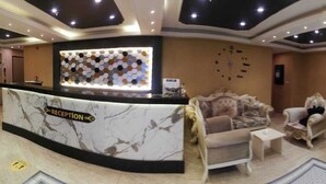 A reception area with a marble counter, sofas, and a television screen. - Royal Palas Hotel (Van)