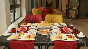 A breakfast setting with a variety of dishes, including bread, fruits, and pastries, arranged on a marble table with red upholstered chairs. - Royal Palas Hotel (Van)