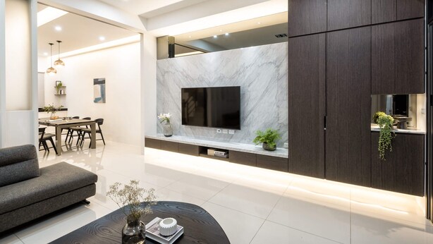 A modern living room with a flat-screen TV mounted on a marble wall, dark wood cabinets, a grey sofa, and a dining area in the background. - Single Eyelid Hostel (Yuanshan)