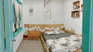Un dormitorio con una cama de madera, una mesita de noche pequeña, un estante en la pared y una puerta con cortinas color turquesa.