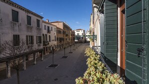 Une rue étroite, bordée de bâtiments des deux côtés, avec une rangée d’arbres et une porte verte sur le côté droit.